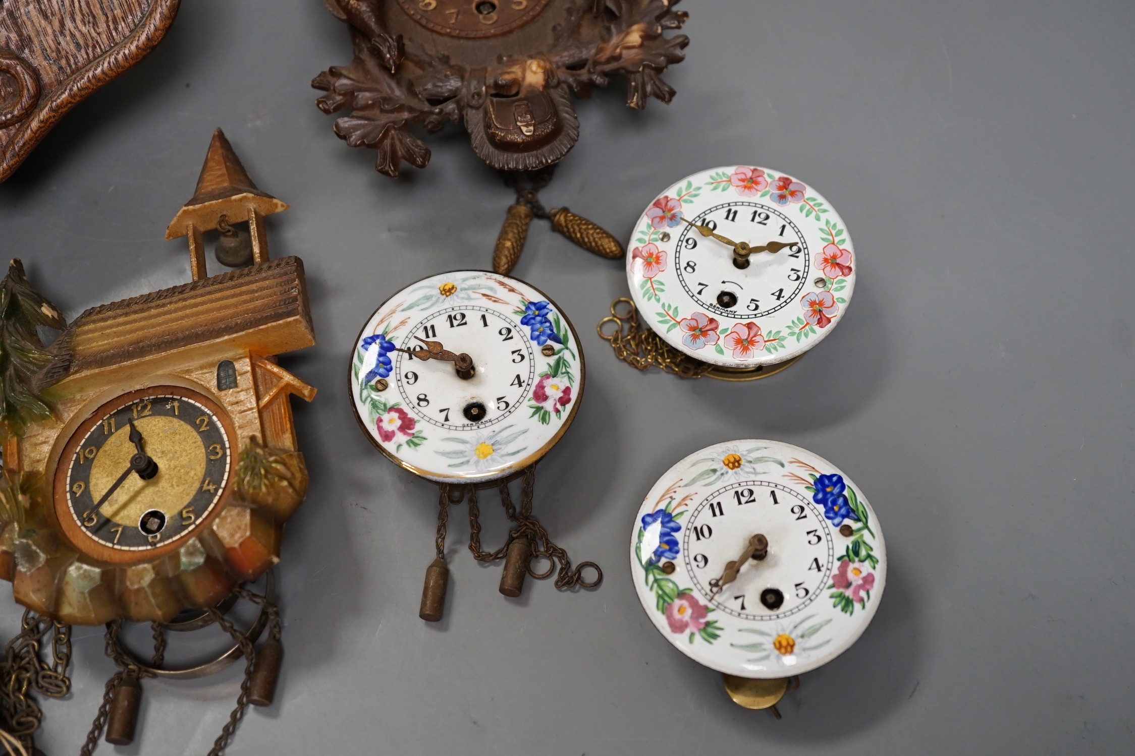 An early 20th century German Jugendstil oak wall timepiece, four miniature Black Forest timepieces and three floral enamelled examples, largest 23cms high